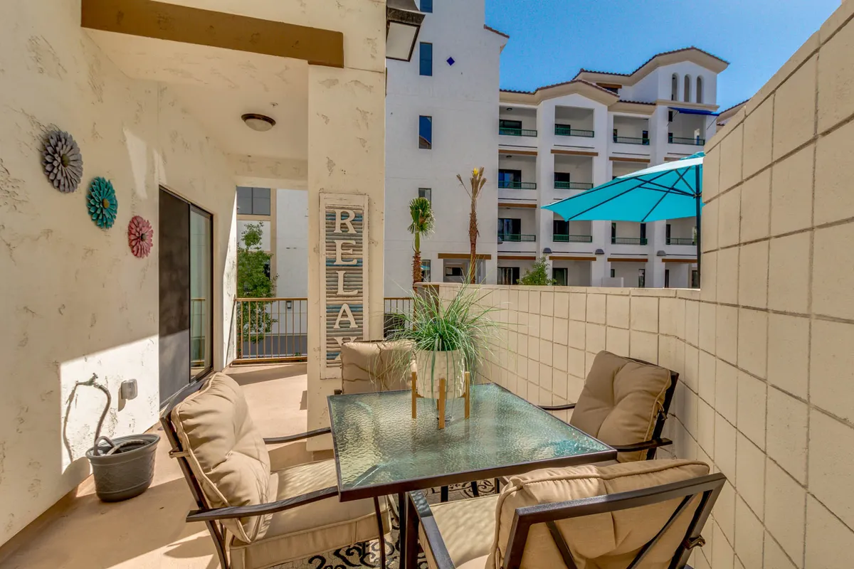 A serene outdoor area with a glass table, comfortable seating, decorative flowers, and an outdoor umbrella. The scene suggests a space for al fresco dining, relaxing, and enjoying beautiful views.