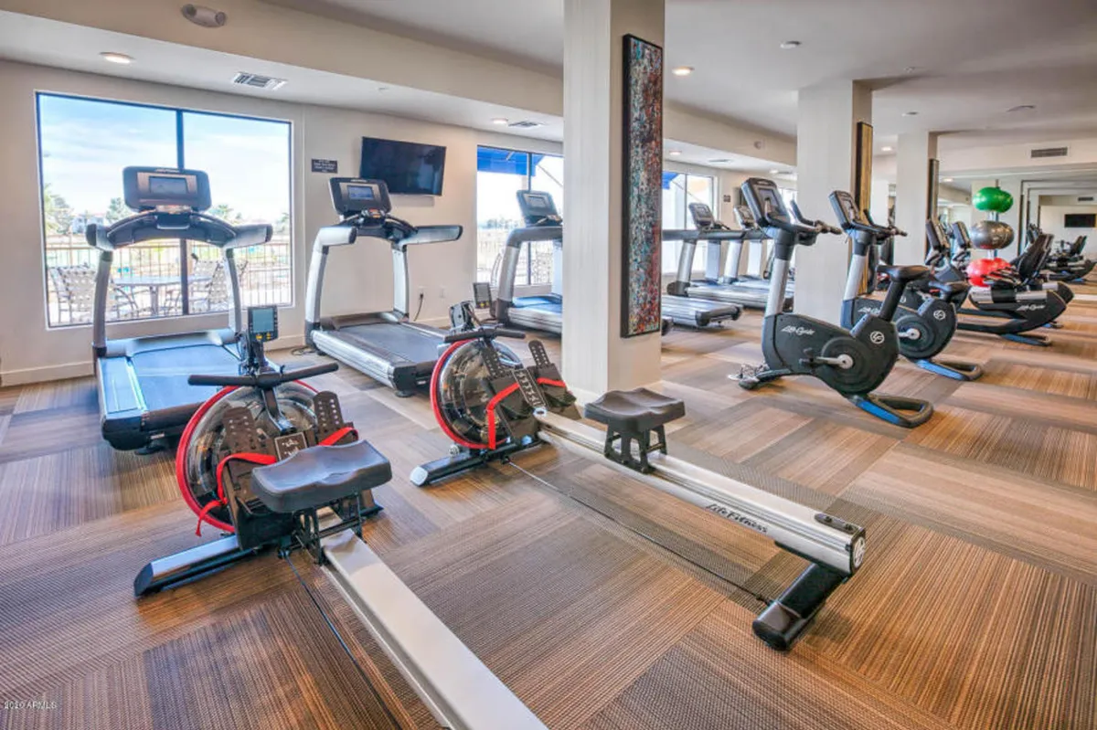 A bright, modern fitness center with large windows, featuring treadmills, rowing machines, and exercise bikes. The open space encourages both personal workouts and community fitness activities.