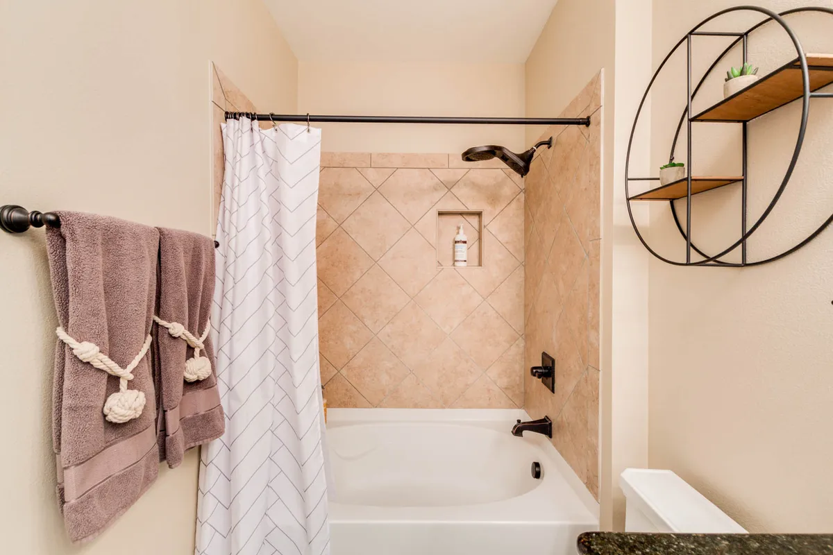 A spa-like bathroom featuring a deep soaking bathtub, fresh towels, and a shelf for toiletries. The neutral color palette and soft lighting create a soothing, luxurious setting perfect for self-care and unwinding.