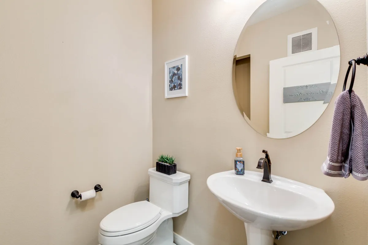 A serene powder room with a round mirror above the sink, elegant fixtures, framed art, and neutral décor. The space feels inviting and functional for guests or quick refreshes.