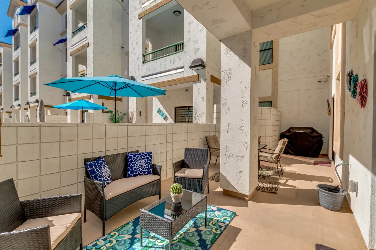 A welcoming outdoor seating area with plush cushions and blue umbrellas, arranged around a coffee table, set in a sun-drenched open space ideal for relaxing or socializing. The inviting setup suggests a perfect spot to unwind after a day of activities.