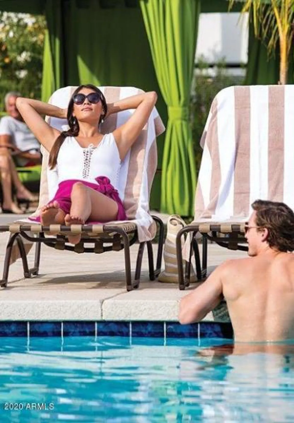A bright resort-style swimming pool scene with lounge chairs, a sunbathing woman, and a man enjoying the water. The setting is casual and inviting, emphasizing leisure, relaxation, and social opportunities in a resort environment.