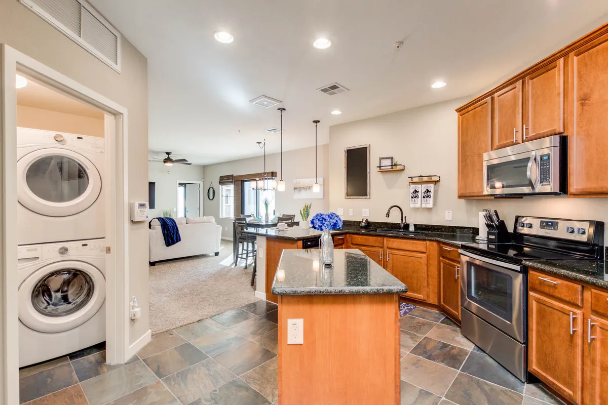 An inviting kitchen and dining space with a prominent granite kitchen island, modern appliances, washer and dryer set, and an adjacent dining area. The layout highlights both style and everyday functionality for meal prep and extended stays.