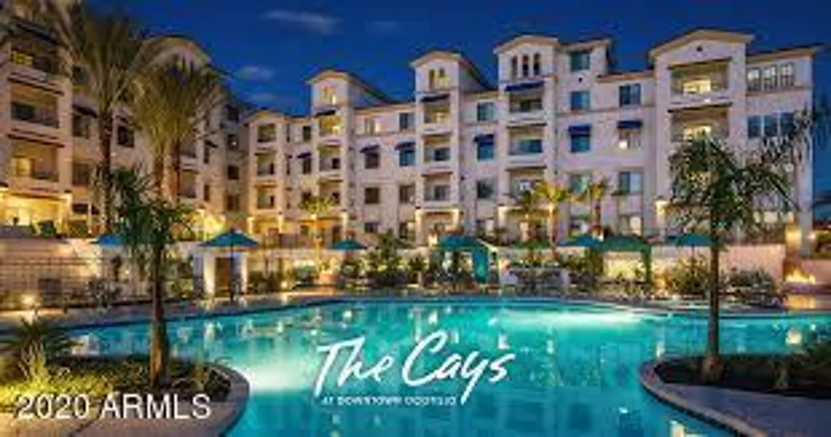A luxurious heated swimming pool is the centerpiece, bordered by palm trees, lounge chairs, and umbrellas. The building facade rises in the background, showcasing the resort-style amenities available on-site for relaxation and after-work enjoyment.