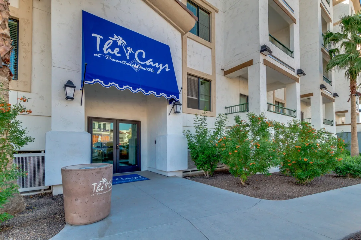 This image captures the blue awning bearing the property name, the entrance door, and lush greenery framing the pathway to the building. The inviting entry is surrounded by well-maintained landscaping, setting a welcoming and professional tone.