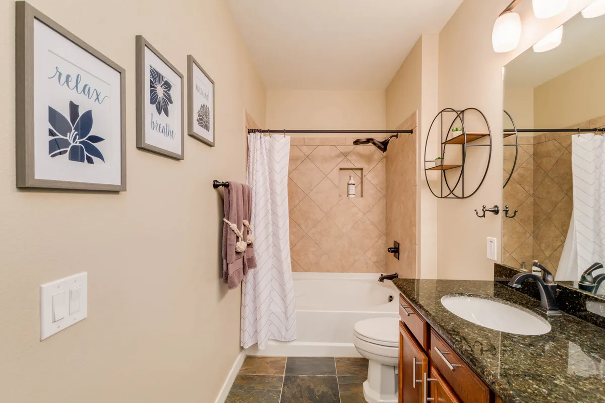 A tranquil bathroom scene featuring a soaking bathtub, a modern vanity with a granite countertop, and textured wall tiles. Framed art and subtle decor touches create a peaceful, inviting environment for relaxation and self-care.