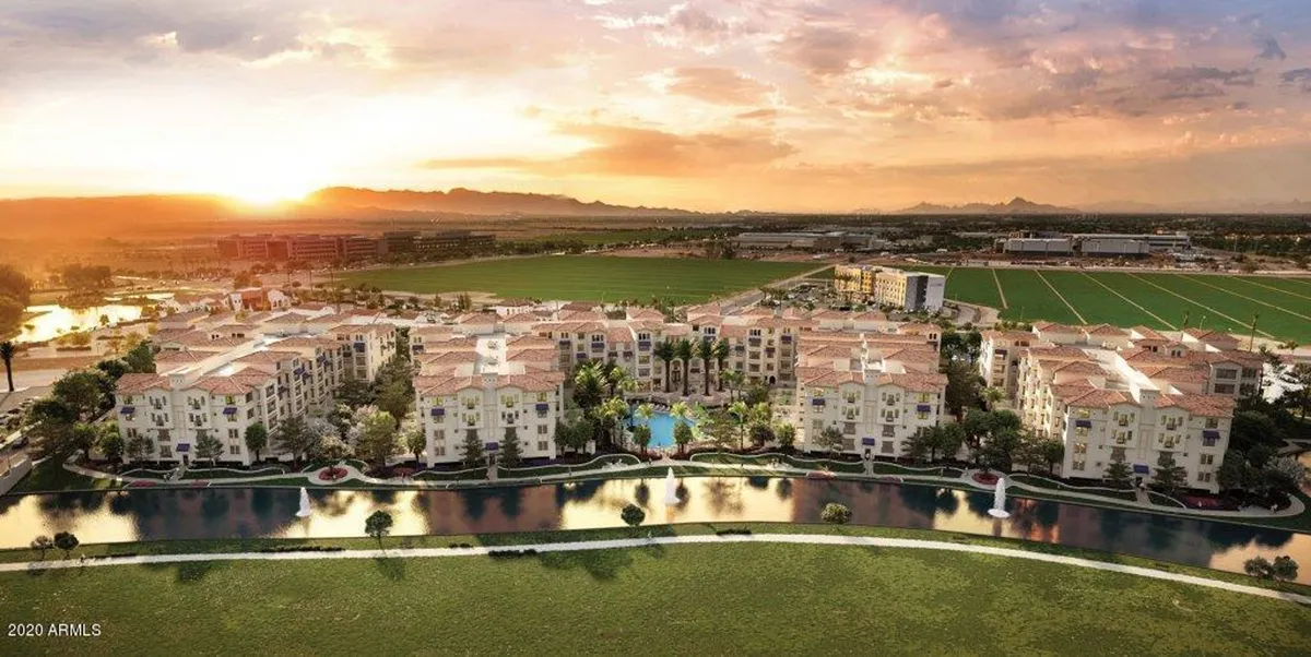 A luxurious exterior view of the resort's main swimming pool, surrounded by landscaped gardens, palm trees, sun loungers, and cabanas. The apartment buildings form an elegant backdrop, and the pool area glows gently under a sunset sky, inviting relaxation and social gatherings.