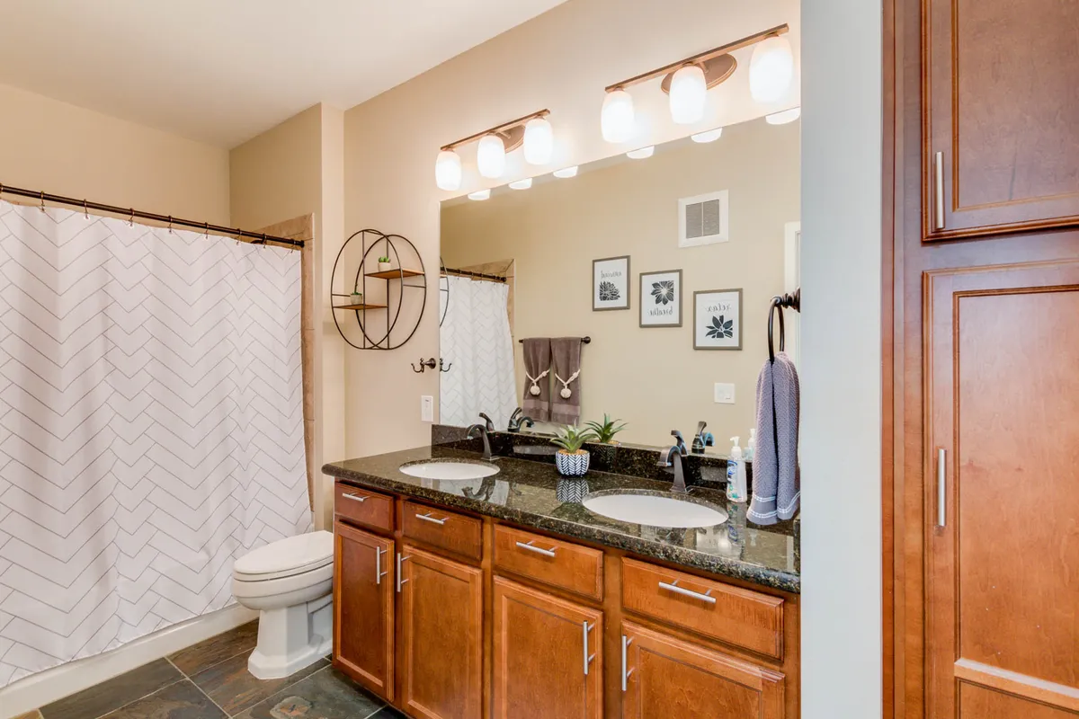 A double-sink granite vanity with sleek fixtures anchors the elegant ensuite bath. Decorative wall art and neatly arranged towels evoke a sense of spa-like tranquility and attention to detail, making the space ideal for rejuvenating morning or evening routines.
